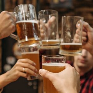 Group of friends clinking beer mugs, enjoying a fun gathering indoors.
